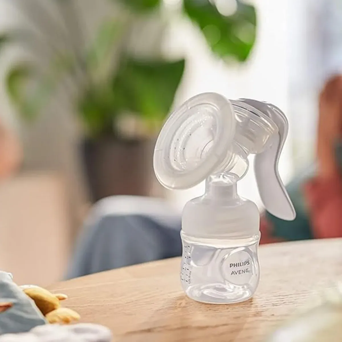 شیردوش دستی فیلیپس اونت با شیشه شیر Natural روی میز چوبی، تصویر در محیط خانه